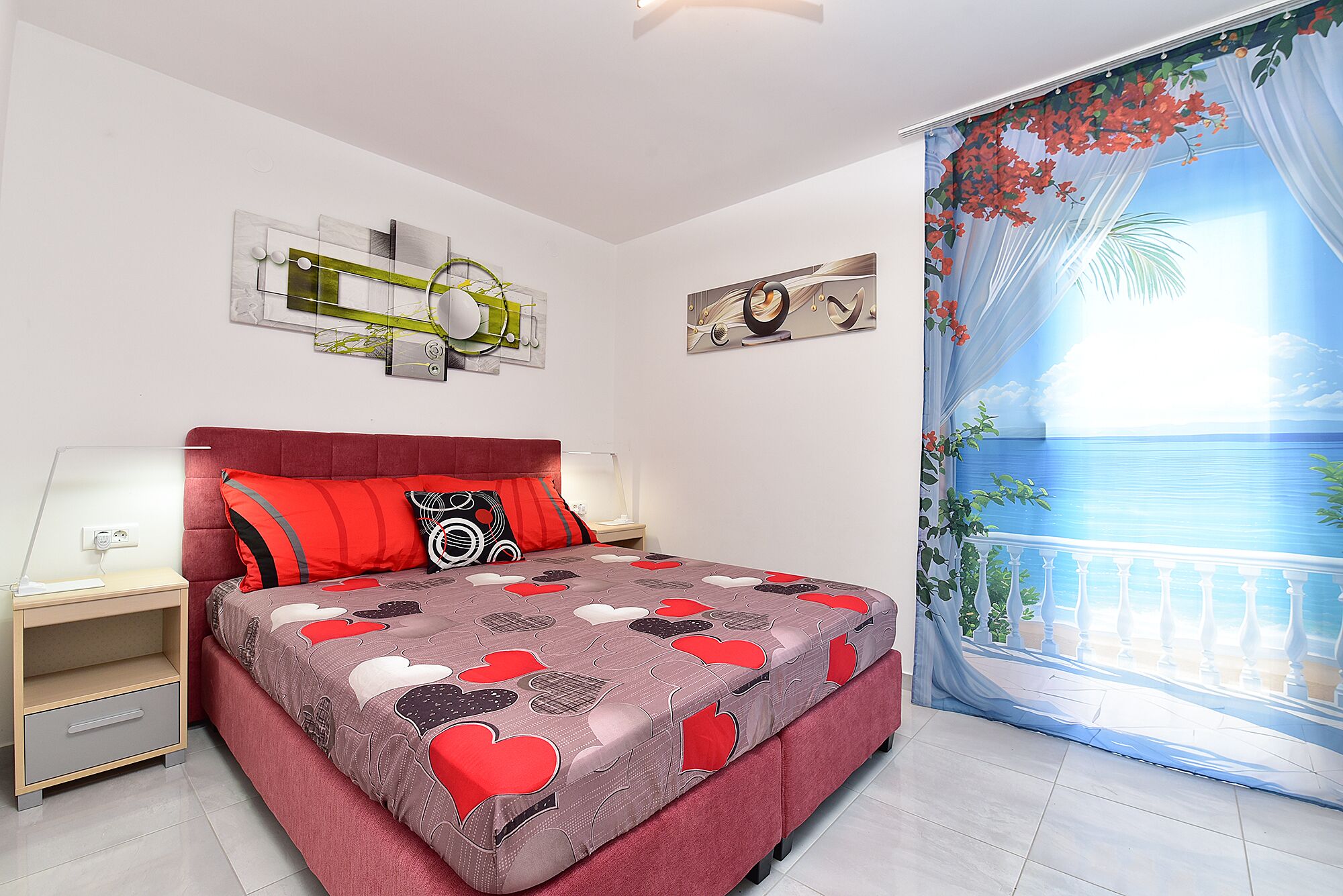 Ein Schlafzimmer mit Bett, Nachttisch, Lampe, Fenster mit Aussicht und Wandbildern.