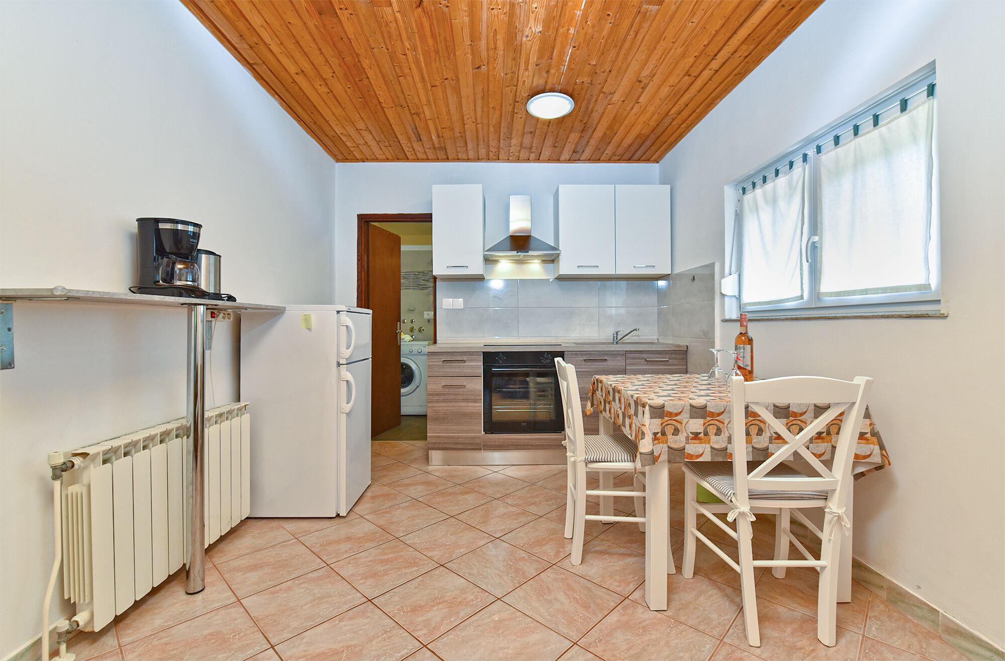 A compact kitchen with a wooden ceiling, a built-in oven, and a dining area with a table and chairs.