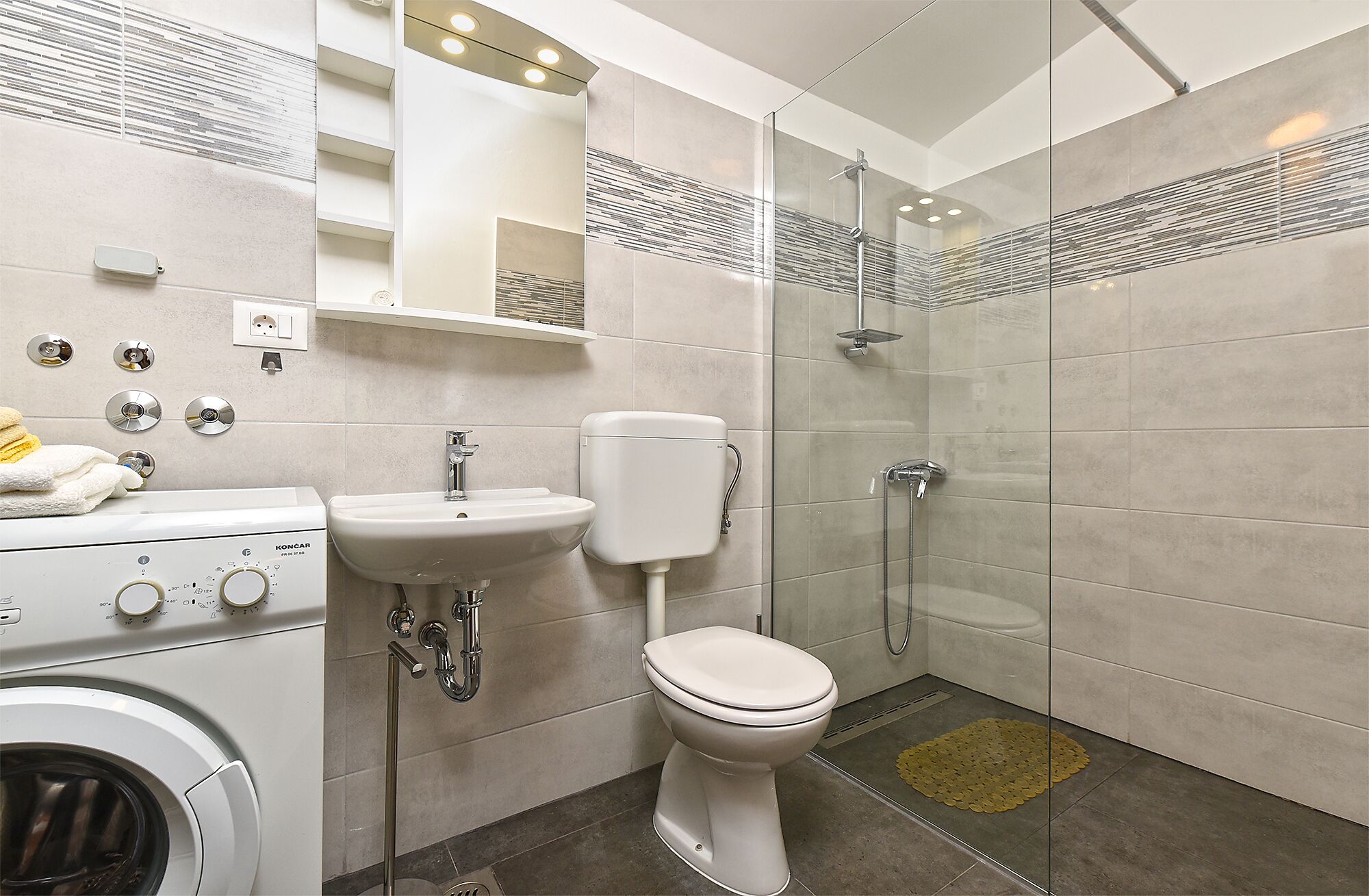 Ein modernes Badezimmer mit Dusche, Toilette, Waschbecken und Waschmaschine.