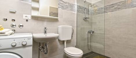 Ein modernes Badezimmer mit Dusche, Toilette, Waschbecken und Waschmaschine.