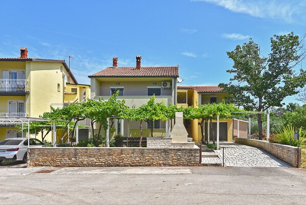 A row of yellow buildings with red-tiled roofs, stone walls, and a paved driveway.
