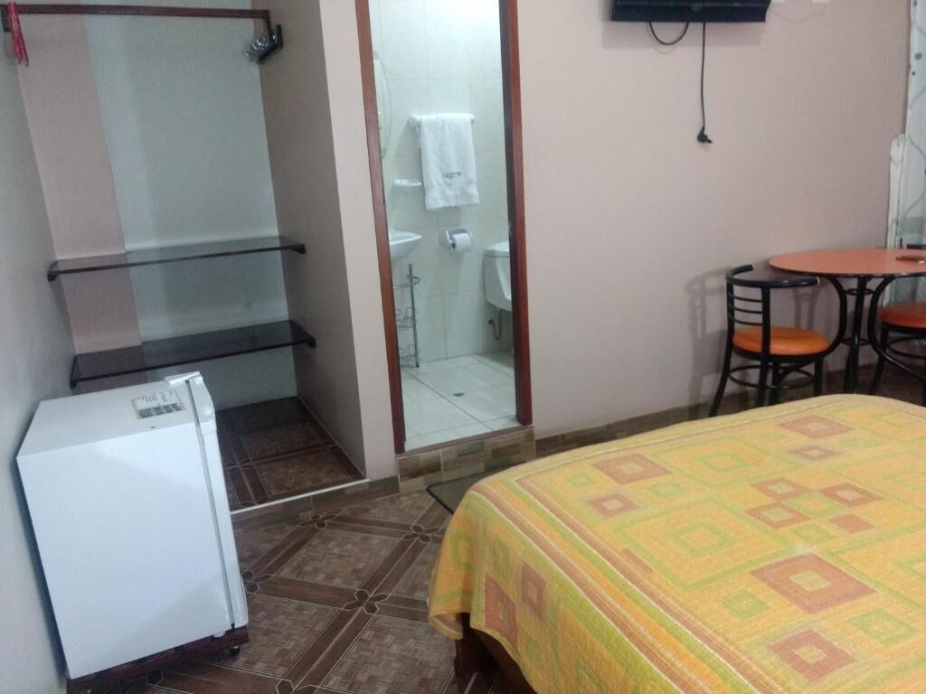 A room with a bed, a small refrigerator, a glass shower enclosure, and a table with chairs.