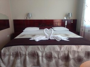 A hotel room with a bed, two bedside lamps, a headboard with the hotel name, and a decorative towel arrangement on the bed. - Hotel El Ensueño (Rupa-Rupa)
