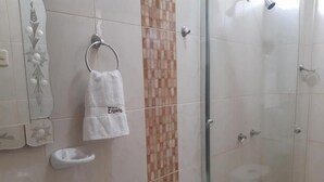 Un baño con inodoro, cabina de ducha de vidrio y una toalla colgada en un aro metálico.