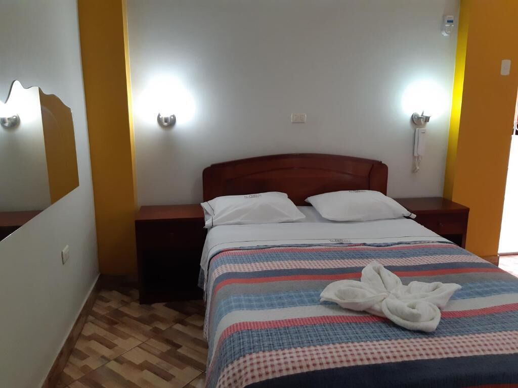 A hotel room with a wooden headboard, a striped bedspread, and a white towel on the bed.