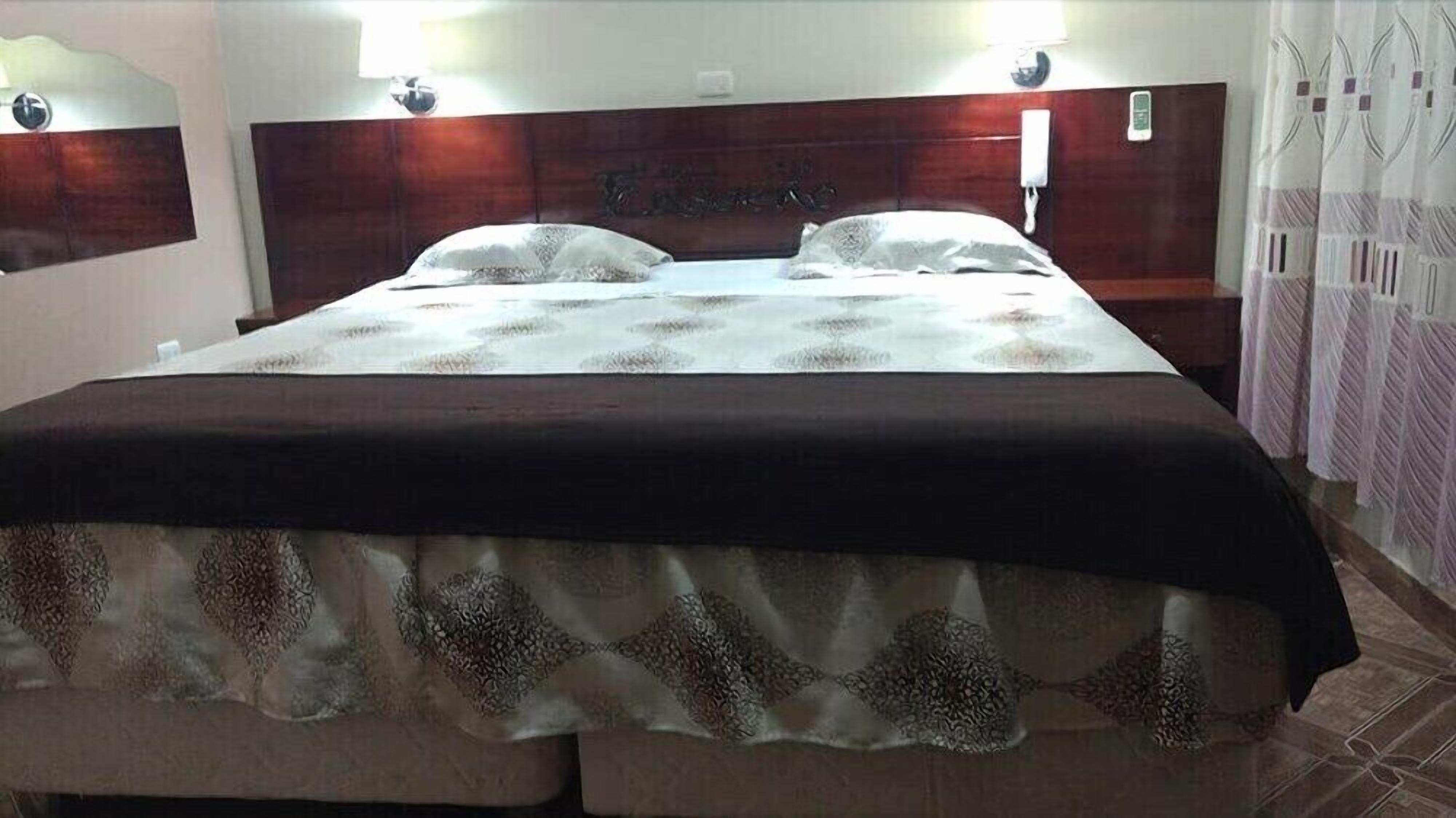 A hotel room with a large bed, a wooden headboard, and a mirror on the wall.