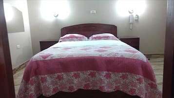 Una cama con colcha y almohadas estampadas con motivos florales, un cabecero de madera y dos mesitas de noche con lámparas.