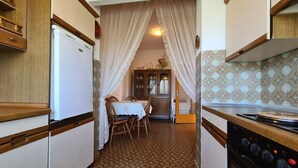 A narrow kitchen with a dining area, wooden cabinets, a stove, and patterned floor tiles. - Apartment 930/2214 (Istria - Valbandon), 1000m from the beach (Valbandon)