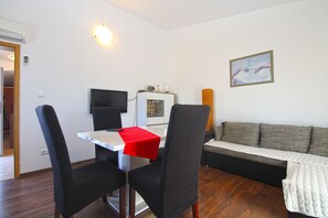 A living room with a white table, black chairs, a red tablecloth, a white sofa, and a painting on the wall.