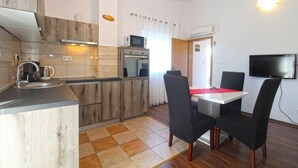 A compact kitchen with a microwave, oven, and coffee maker. There is a dining area with a table and chairs, and a TV mounted on the wall.