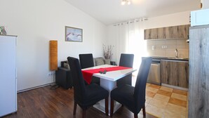 A compact kitchen with a dining area, featuring a white table with a red tablecloth, black chairs, and a wooden cabinet.