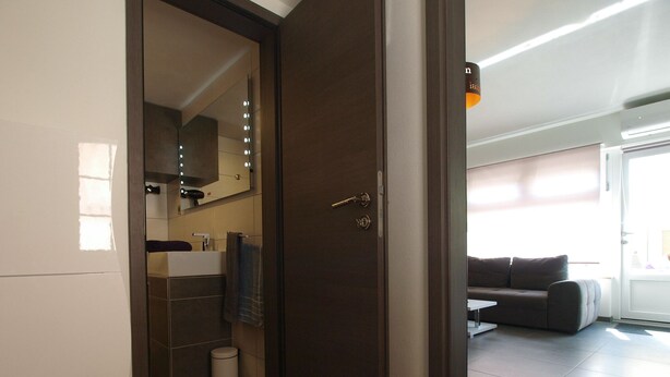 A modern bathroom with a dark wooden door, a mirror with lights, a white sink, and a towel hanging on the wall. - Apartment 934/23284 (Istria - Fažana), 500m from the beach (Fažana)