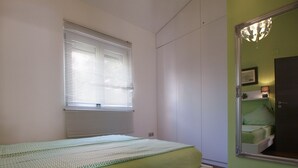 A bedroom with a bed, a window with blinds, a mirror, and a nightstand with a lamp. - Apartment 934/23284 (Istria - Fažana), 500m from the beach (Fažana)