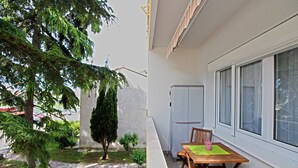 A patio with a wooden table and chairs, a small garden with a tree and shrubs, and a white wall with a window.