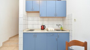 A small kitchen with blue cabinets, a white countertop, a kettle, and a sink.