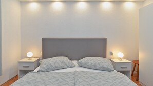 A neatly made bed with a geometric patterned bedspread, two bedside tables with illuminated lamps, and a headboard with built-in lighting.