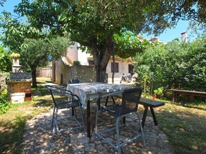 Une terrasse extérieure avec une table et des chaises, entourée d’arbres et d’un mur en pierre.