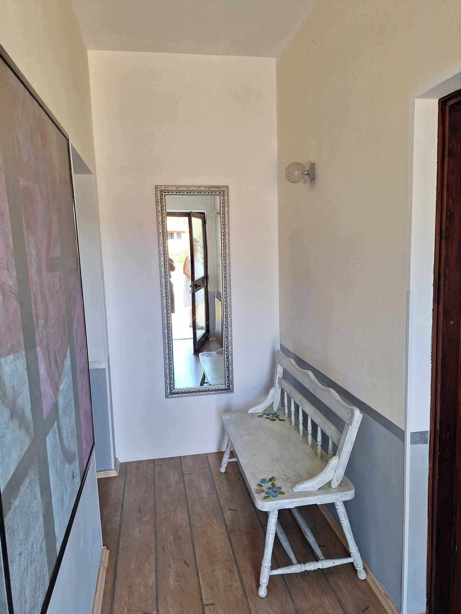 Un couloir étroit avec un banc en bois et un grand miroir accroché au mur.