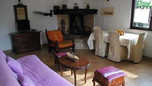 Una sala de estar acogedora con chimenea, un sofá, una mesa de comedor con sillas y un pequeño armario de madera.