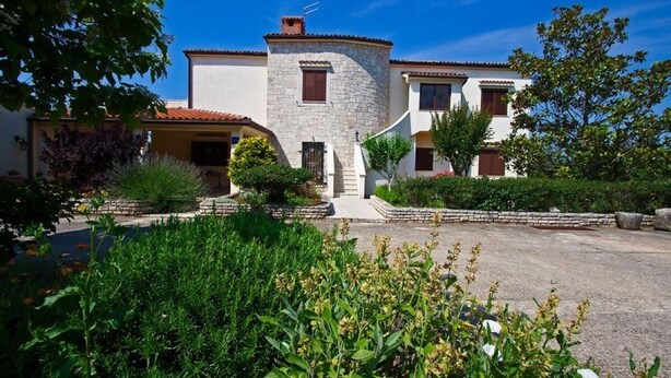 A two-story building with a stone tower, surrounded by lush greenery and a paved driveway.