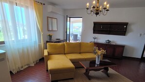 A living room with a yellow sofa, a wooden coffee table, and a chandelier.