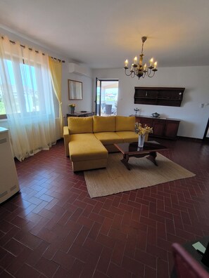 A living room with a yellow sofa, a wooden coffee table, and a chandelier.