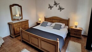 A bedroom with a wooden bed, two bedside tables with lamps, a dresser, a mirror, and wall art.