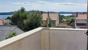 A balcony with a view of a lake, houses with red-tiled roofs, and greenery.