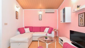 A living room with a pink wall, a white sofa, a glass coffee table, a flat-screen TV, and a white cabinet.