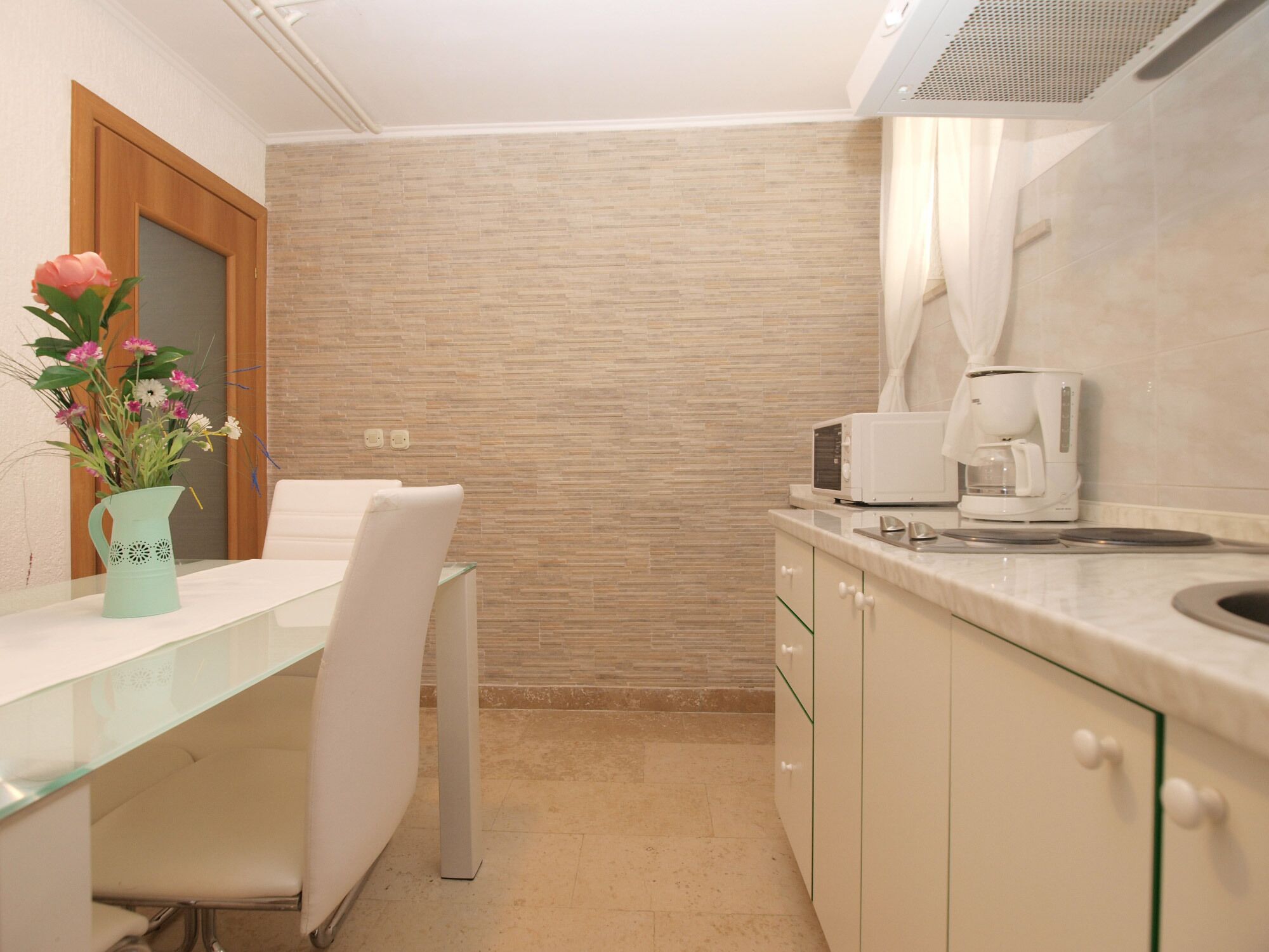 A modern kitchen with a marble countertop, a coffee maker, and a vase with flowers on the table.