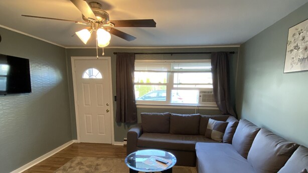 A living room with a ceiling fan, a glass coffee table, a brown sofa, and a door. - 2 bedrooms with shared pool. apt1 (Hampton)