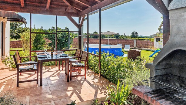 Una terrazza esterna con tavolo e sedie, un barbecue e una piscina sullo sfondo.
