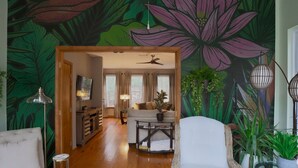 A living room with a large floral mural, a sofa, a coffee table, and a dining area with a chandelier.