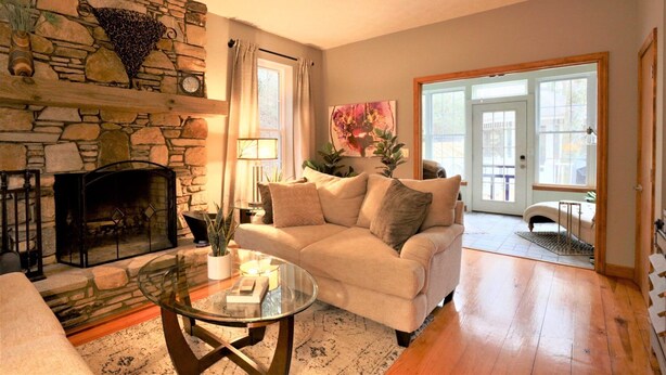 A living room with a stone fireplace, a sofa, a glass coffee table, and a large window.