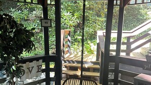 A wooden deck with a wicker chair and a small table, a sign with 'LOVE' visible, and a view of a wooden staircase and greenery.