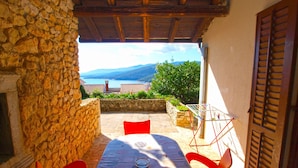 Un patio con paredes de piedra, una mesa y sillas, con vistas panorámicas a un lago y montañas.