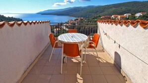 A balcony with a round table and orange chairs, overlooking a coastal landscape with houses and a sea view. - Apartment 981/2644 (Istria - Rabac), 500m from the beach (Rabac)