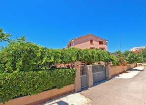 A two-story building with a gated entrance, surrounded by lush greenery and a clear blue sky. - Apartment 994/3137 (Istria - Fažana), 350m from the beach (Fažana)