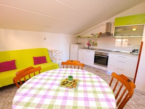 A compact kitchen with white cabinets, a green countertop, and a dining area with a checkered tablecloth. - Apartment 994/3137 (Istria - Fažana), 350m from the beach (Fažana)