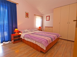 A bedroom with a wooden bed, two bedside tables with lamps, a wardrobe, and a window with curtains. - Apartment 1002/3282 (Istria - Fažana), 900m from the beach (Fažana)