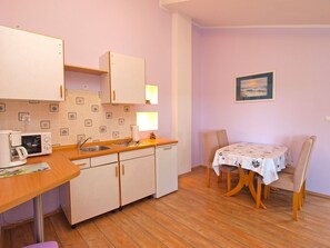 Cozinha compacta com pia, micro-ondas e armários, uma mesa de jantar com cadeiras e um quadro fixado na parede.