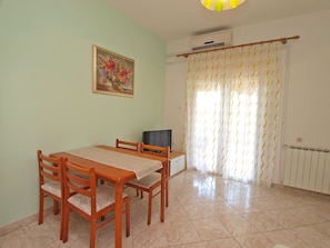 A dining area with a table and chairs, a painting on the wall, and a window with curtains.