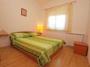 Un dormitorio con cama, mesita de noche, lámpara, ventana con cortinas y radiador.