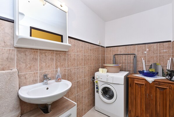 Een badkamer met een wastafel, spiegel, wasmachine en een houten kastje.