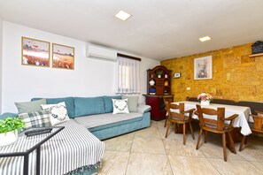 A living room with a sofa, dining table, chairs, a cabinet, and wall-mounted air conditioning.