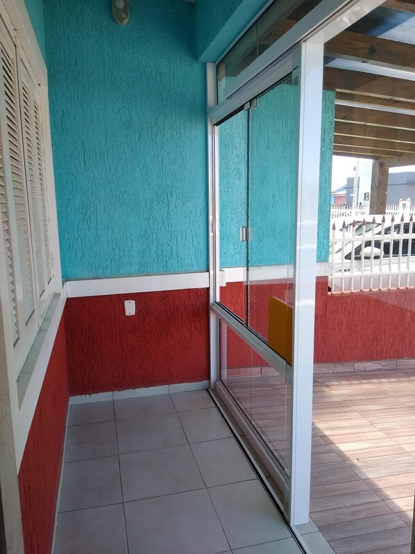 Een hoek van een kamer met een wand in groenblauw en rood, een glazen deur, en een witte hekken buiten.