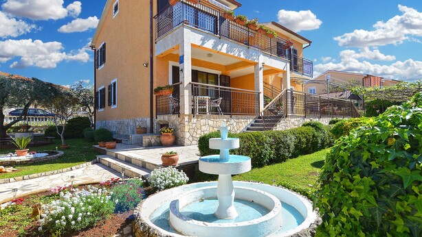 A two-story house with a balcony, a fountain, and a garden.