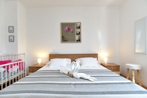 Un letto rifatto con lenzuola a righe, due comodini con lampade, una culla con biancheria rosa e un'opera d'arte appesa al muro.