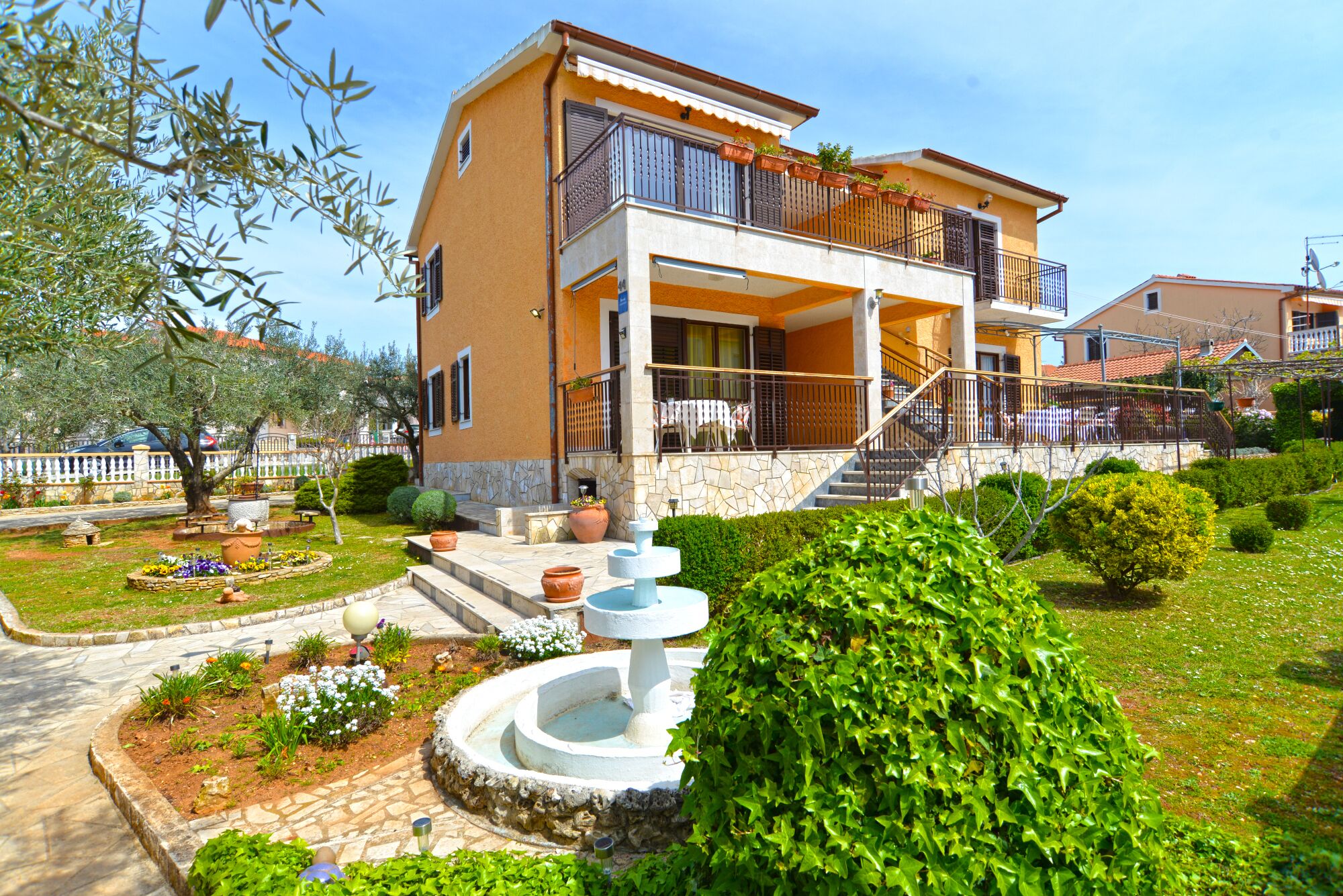 Una casa a due piani con un balcone, una scala in pietra e un giardino con una fontana.