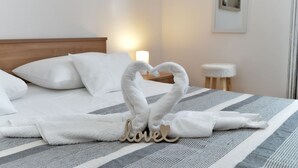 Ein ordentlich bezogenes Bett mit weißen Kissen, einer gestreiften Decke und einem Handtuch, das zu einem Herz geformt ist, mit dem Wort 'love' darauf.